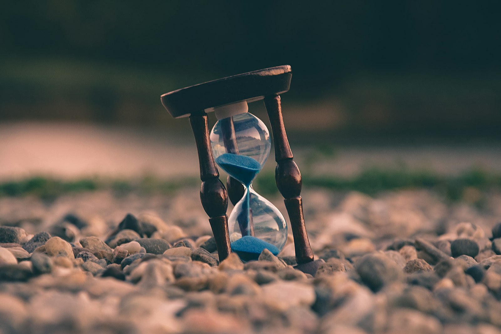 An hourglass with blue sand standing on a pebble beach