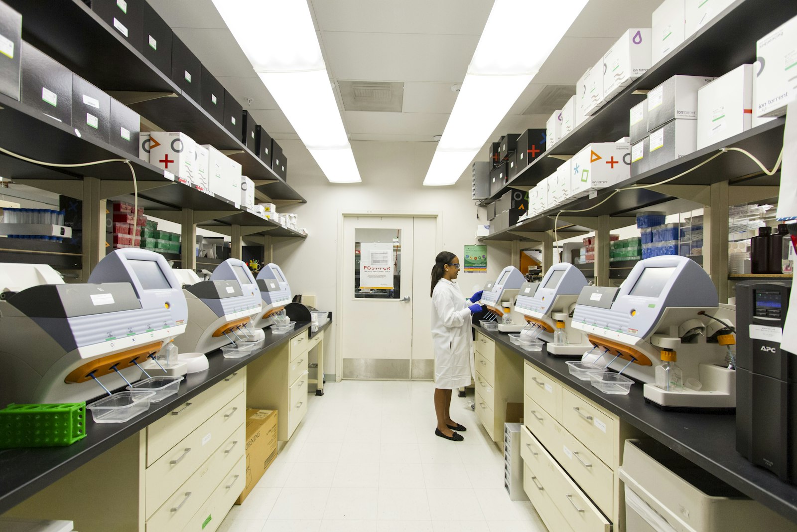 A laboratory technician working at a bench of analyzers in a clinical lab